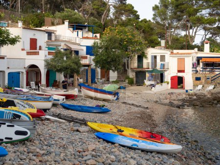 Téléchargez les photos : Homme regardant le mobile à Cala s'Alguer, avec des bateaux et des planches de surf. Maisons de pêcheurs typiques avec portes et fenêtres colorées, Palamos, Espagne. - en image libre de droit