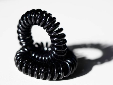 Black telephone wire hair tie on white background. Beauty concept