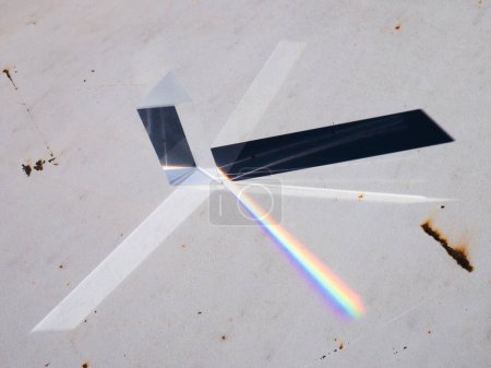 Photo for Scattering of a ray of sunlight (white light) through a prism creating refraction on a grungy white plate, reflection and decomposition of light in the colors of the rainbow. - Royalty Free Image
