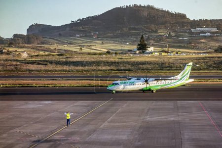 Foto de Tenerife, España; 23-04-2024: Avión de hélice de la compañía Binter y el ATR 72-600 siendo indicado por el personal de pista en las maniobras previas al despegue en el aeropuerto Tenerife Norte - Imagen libre de derechos