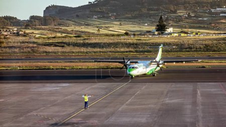 Foto de Tenerife, España; 23-04-2024: Avión de hélice de la compañía Binter y el ATR 72-600 siendo indicado por el personal de pista en las maniobras previas al despegue en el aeropuerto Tenerife Norte - Imagen libre de derechos