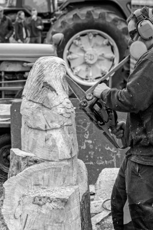 Photo for Male sculptor at The Nidderdale Show wearing headphones and a face mask while using a chainsaw to carve an owl out of wood, Pateley Bridge, Yorkshire, UK. - Royalty Free Image