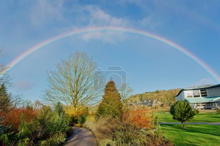 Ein lebendiger Regenbogen ziert den Himmel über RHS Garden, Harrogate, England, an einem sonnigen Wintertag und verleiht der Szene eine ätherische Schönheit..