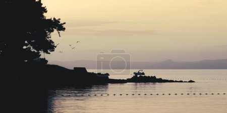 Photo for Dawn in the Adriatic Sea. Seagulls flying on a background of mountains and boats. - Royalty Free Image