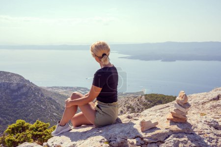 Photo for The girl sits at the edge of the cliff and looks into the distance. - Royalty Free Image