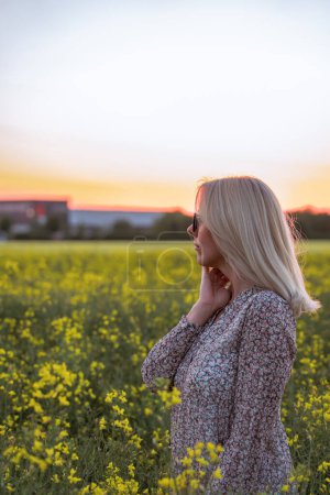 Foto de Girl in a dress in the middle of a field with yellow flowers, at sunset - Imagen libre de derechos