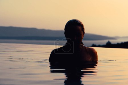 Foto de Girl at sunset in the pool. In the background, the sea and mountains. - Imagen libre de derechos