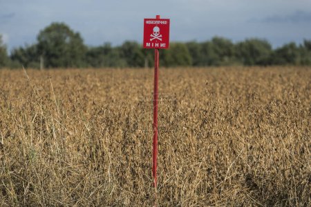 Una señal de advertencia con la inscripción en Ucrania PELIGROSO - MÍO se instala en un campo de agricultores en el norte de Ucrania. Foto de alta calidad