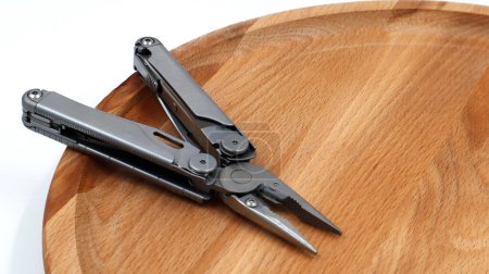 Foto de Un moderno cuchillo multifuncional plegable abierto hecho de hierro gris sobre un fondo de madera. Multiherramienta con herramientas extendidas y alicates. Producto compacto y portátil. Cuchillo de bolsillo. Concepto EDC - Imagen libre de derechos