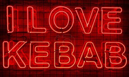 Neon shining sign in red color on a brick wall in the dark with the inscription or slogan I love kebab. Brick wall, background. Bright electric neon light. Cafe-restaurant Doner Kebab