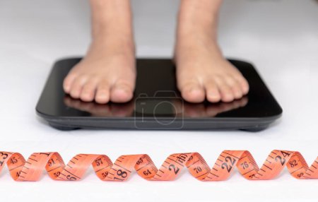 Foto de A Body Measuring Tape or Soft Measuring Tape Ruler with a person on a scale on the background. Concept: Weight loss - Imagen libre de derechos