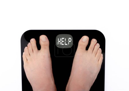 Foto de A person standing on a scale and showing the word HELP on the screen of a digital scale. Concept: Weight Loss - Imagen libre de derechos