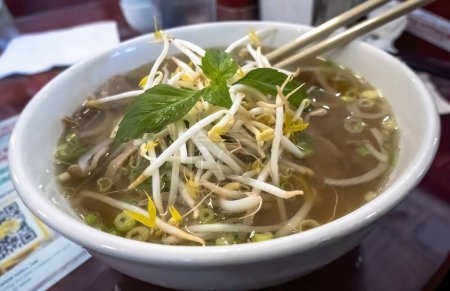 Photo for Pho a Vietnamese soup dish consisting of broth, rice noodles, herbs, and meat. A popular food in Vietnam where it is served in households, street-stalls, and restaurants country-wide. - Royalty Free Image
