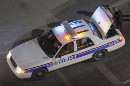 Foto de Calgary, Alberta, Canadá. Jun 10, 2023. Mirando desde arriba, un vehículo de la policía de Calgary con la puerta trasera abierta, como un oficial responde a una llamada de emergencia en el centro de Calgary por la noche. - Imagen libre de derechos