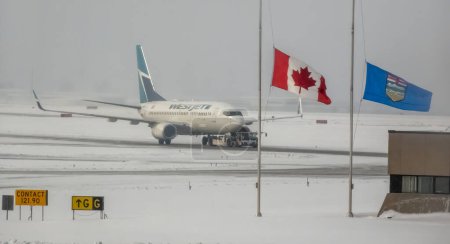 Foto de Calgary, Alberta, Canadá. Mar 22, 2024. Un avión Westjet con bandera canadiense y Albertan a medio mástil durante el invierno. - Imagen libre de derechos