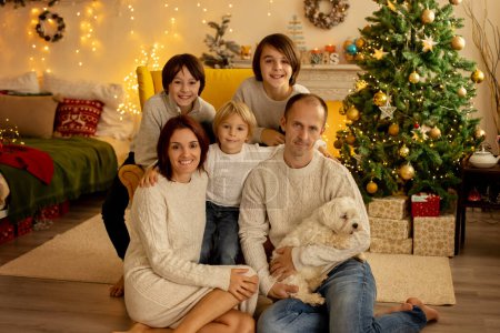 Téléchargez les photos : Joyeux famille avec trois enfants et chien, assis à la maison à Noël, ambiance chaleureuse, période de Noël - en image libre de droit