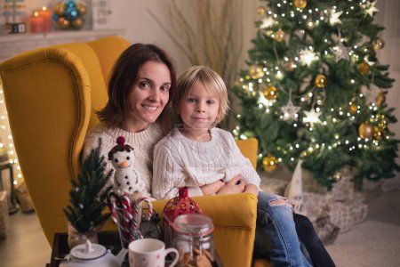 Foto de Lindo niño, niño, sentado en un sillón amarillo en una habitación decorada para Navidad con la madre y la abuela - Imagen libre de derechos