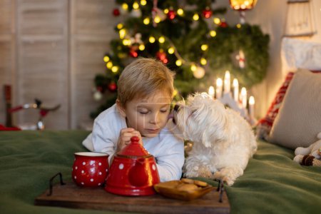 Foto de Lindo niño preescolar, niño rubio con perro mascota, jugando en la habitación de Navidad decorada en casa - Imagen libre de derechos