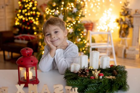 Téléchargez les photos : Mignon enfant d'âge préscolaire, garçon blond, faire la couronne de l'avent à la maison dans la chambre de Noël décorée à la maison - en image libre de droit