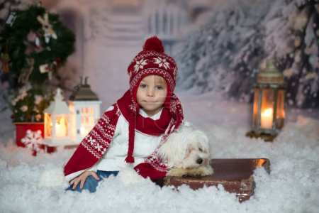 Téléchargez les photos : Enfant blond en bas âge avec des vêtements de Noël, marchant dans la neige, jouant avec un jouet tricoté - en image libre de droit