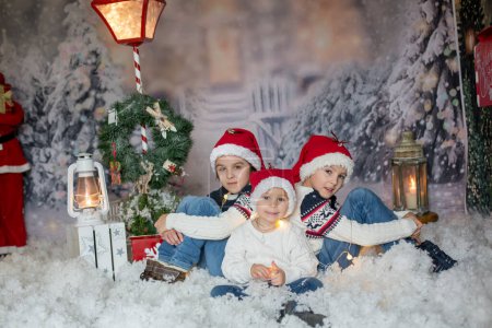 Foto de Niños, sentados en la nieve, envueltos en papel higiénico y cadenas de luz navideñas, mirando a la cámara - Imagen libre de derechos