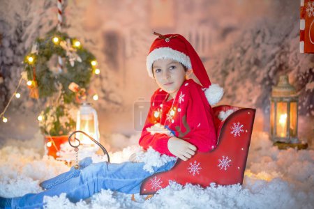 Photo for Cute child, school boy, opening present for christmas, decoration around him, outdoor shot, outdoor snow shot - Royalty Free Image