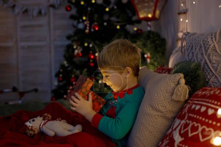 Téléchargez les photos : Mignon enfant d'âge préscolaire, garçon blond avec chien de compagnie, ouverture cadeaux à la maison, chambre de Noël décorée à la maison - en image libre de droit