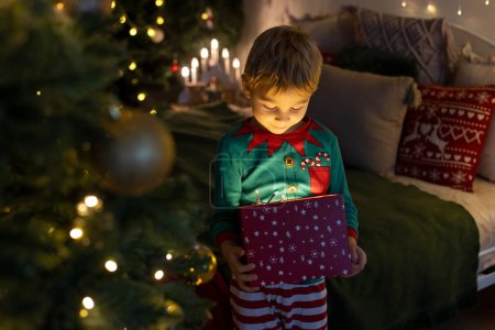 Foto de Lindo niño preescolar, niño rubio con perro mascota, regalos de apertura en casa, decorado habitación de Navidad en casa - Imagen libre de derechos