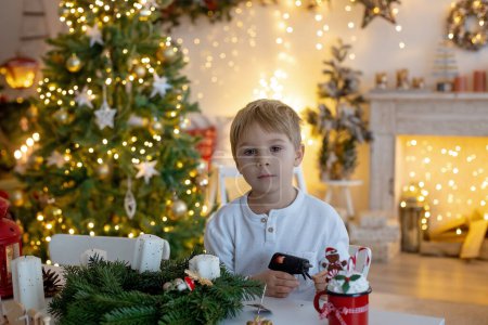 Photo for Cute preschool child, blond boy, making advent wreat at home in decorated Christmas room at home - Royalty Free Image