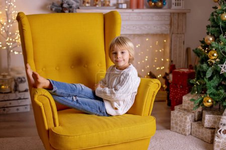 Foto de Lindo niño, niño, sentado en un sillón amarillo en una habitación decorada para Navidad con la madre y la abuela - Imagen libre de derechos