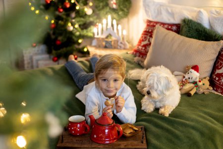 Téléchargez les photos : Mignon enfant d'âge préscolaire, garçon blond avec chien de compagnie, jouer dans la chambre de Noël décorée à la maison - en image libre de droit