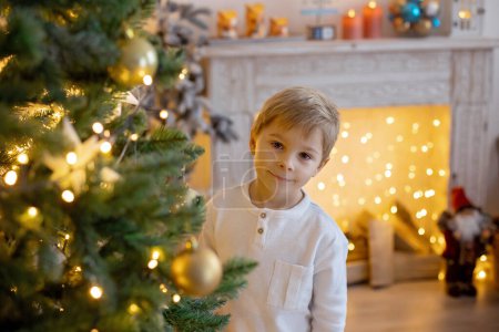 Téléchargez les photos : Mignon enfant d'âge préscolaire, garçon blond avec chien de compagnie, jouer dans la chambre de Noël décorée à la maison - en image libre de droit