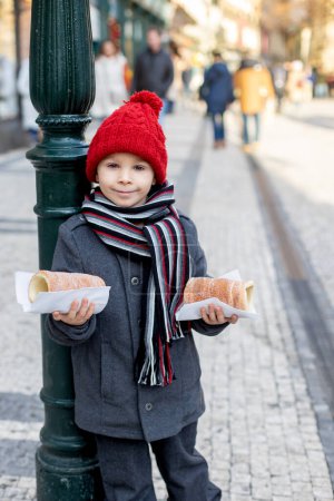 Foto de Child in Prague on Christmas, cute boy, eating traditional czech pastry dough sweet called trdelnik, smiling - Imagen libre de derechos