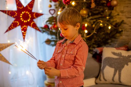 Photo for Child holding sparkler at home at New Years Eve, enjoying happy evening with family - Royalty Free Image