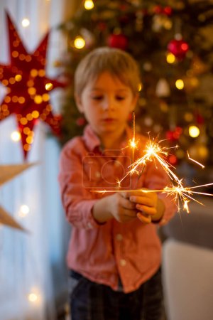 Photo for Child holding sparkler at home at New Years Eve, enjoying happy evening with family - Royalty Free Image