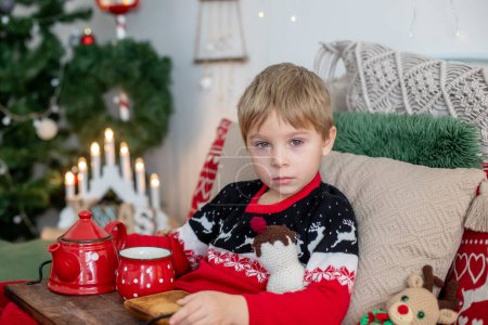 Foto de Small toddler child, lying sick in bed, red eyes, drinking tea on christmas at home - Imagen libre de derechos