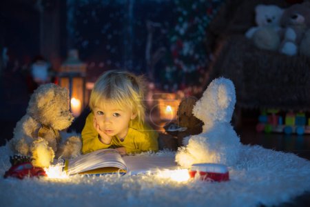 Photo for Sweet toddler boy, reading book at home at night on Christmas night - Royalty Free Image