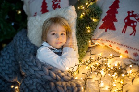 Photo for Toddler child, cute blond boy, sleeping in bed at night with christmas lights around him - Royalty Free Image
