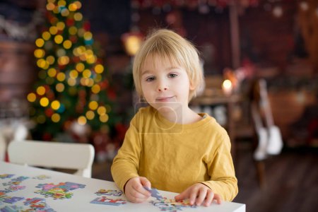 Téléchargez les photos : Enfant blond, tout-petit garçon, s'amuser à la maison à Noël, assembler des puzzles, profiter d'une journée ensoleillée - en image libre de droit
