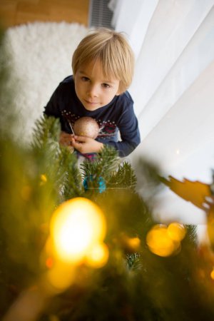 Photo for Cute toddler bchild, boy, decorating christmas tree with toys - Royalty Free Image