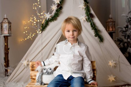 Téléchargez les photos : Enfant tout-petit mignon, garçon, jouant en studio avec neige, tente et lampadaires, décoration de Noël autour de lui - en image libre de droit