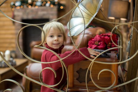 Photo for Blond toddler child, reading book and holding presents in a cozy cottage in the mountains, Christmas time - Royalty Free Image