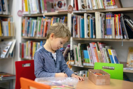 Photo for Adorable little child, boy, sitting in library, reading book and choosing what to lend, kid in book store - Royalty Free Image