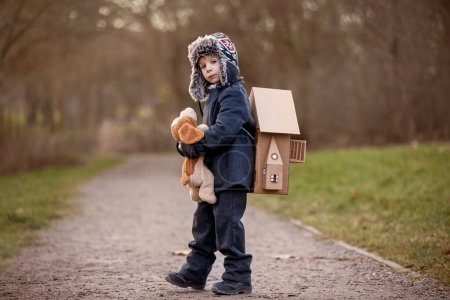 Foto de Little child, blond boy with pet dog, carying home on his back, kid, having paper house, emotional shot - Imagen libre de derechos
