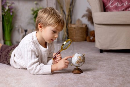 Foto de Cute little toddler blond child, boy, exploring world globe with magnigying glass, learning continents - Imagen libre de derechos