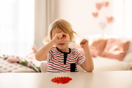 Photo for Cute little child, toddler boy, eating alfa omega 3 child suplement vitamin pills at home for better imunity - Royalty Free Image