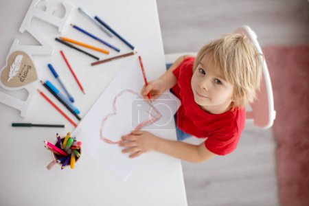 Téléchargez les photos : Enfant tout-petit blond, dessin avec coeur pour la Saint-Valentin, cadeau pour maman, cadeau pour maman pour la fête des mères - en image libre de droit