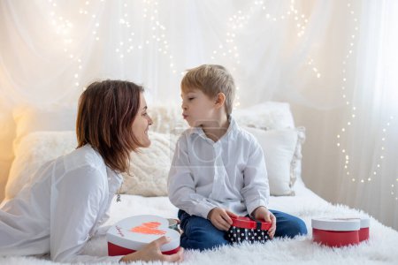 Téléchargez les photos : Cute blonde toddler child, boy, cuddling  in mother, sitting on the bed, pure white background with yellow soft lights - en image libre de droit