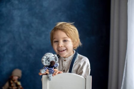 Téléchargez les photos : Mignon portirait de blond préscolaire enfant, garçon, sur fond bleu, tenant jouet - en image libre de droit