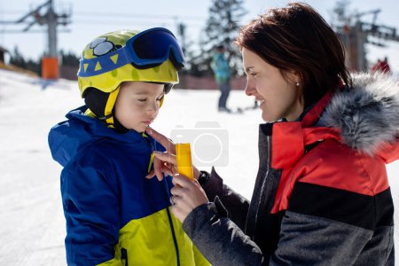 Madre, la aplicación de crema solar en su hijo de esquí, la familia en las vacaciones de esquí de invierno, el esquí, tomar medidas contra el sol duro en las montañas